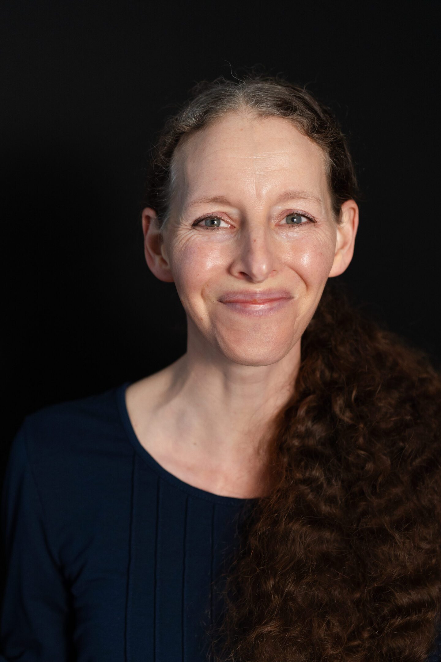 Portrait of a smiling woman with curly hair against a black background.
