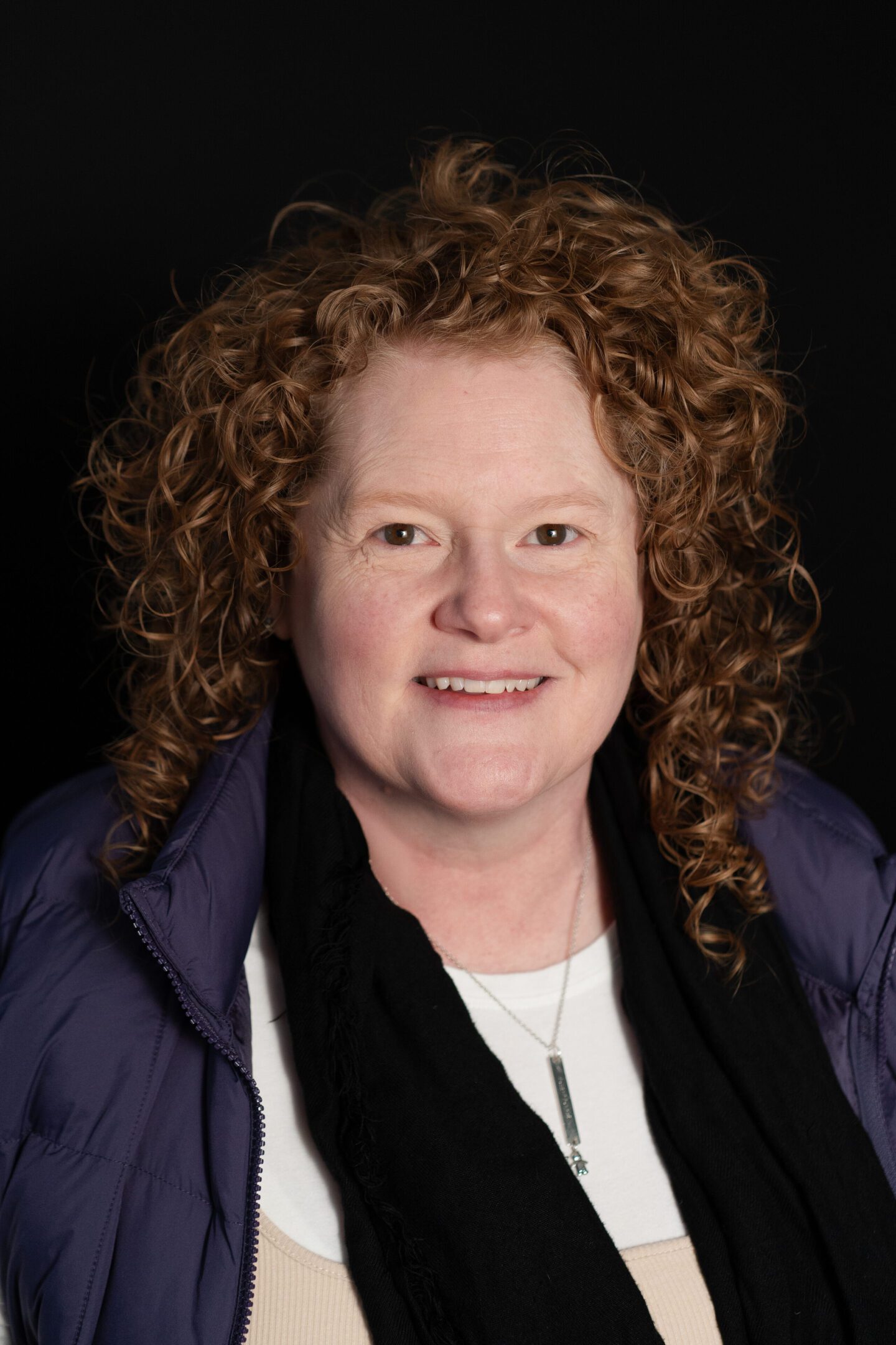 Smiling woman with curly red hair in a dark jacket and scarf.