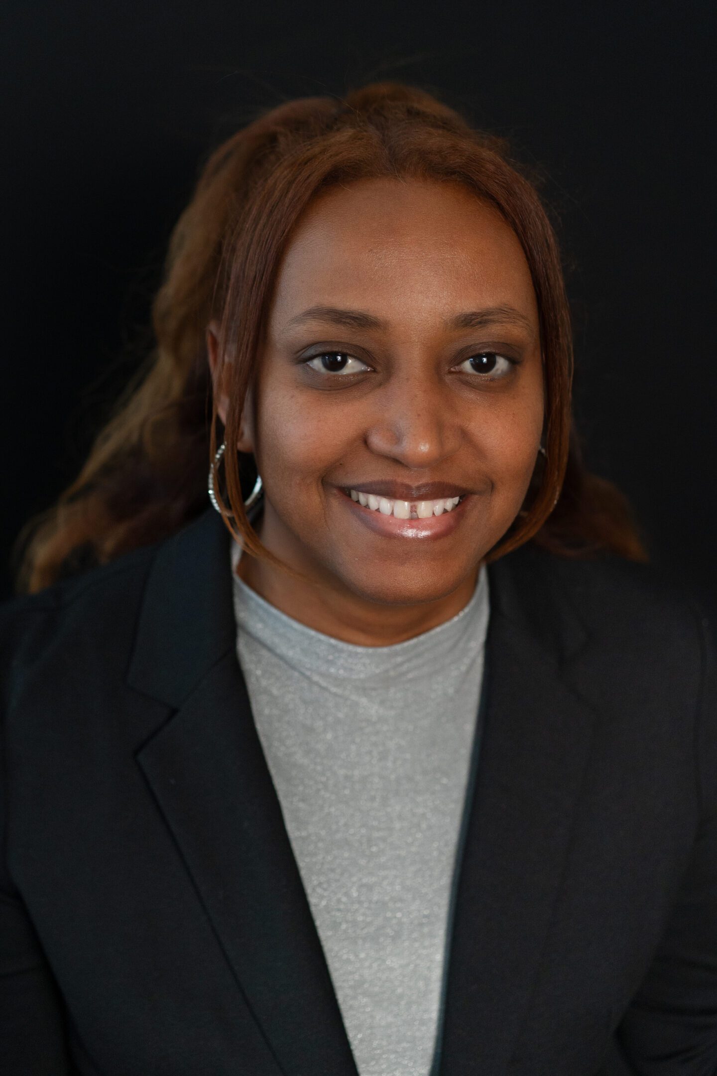 Smiling woman in professional attire with a black blazer and gray top.