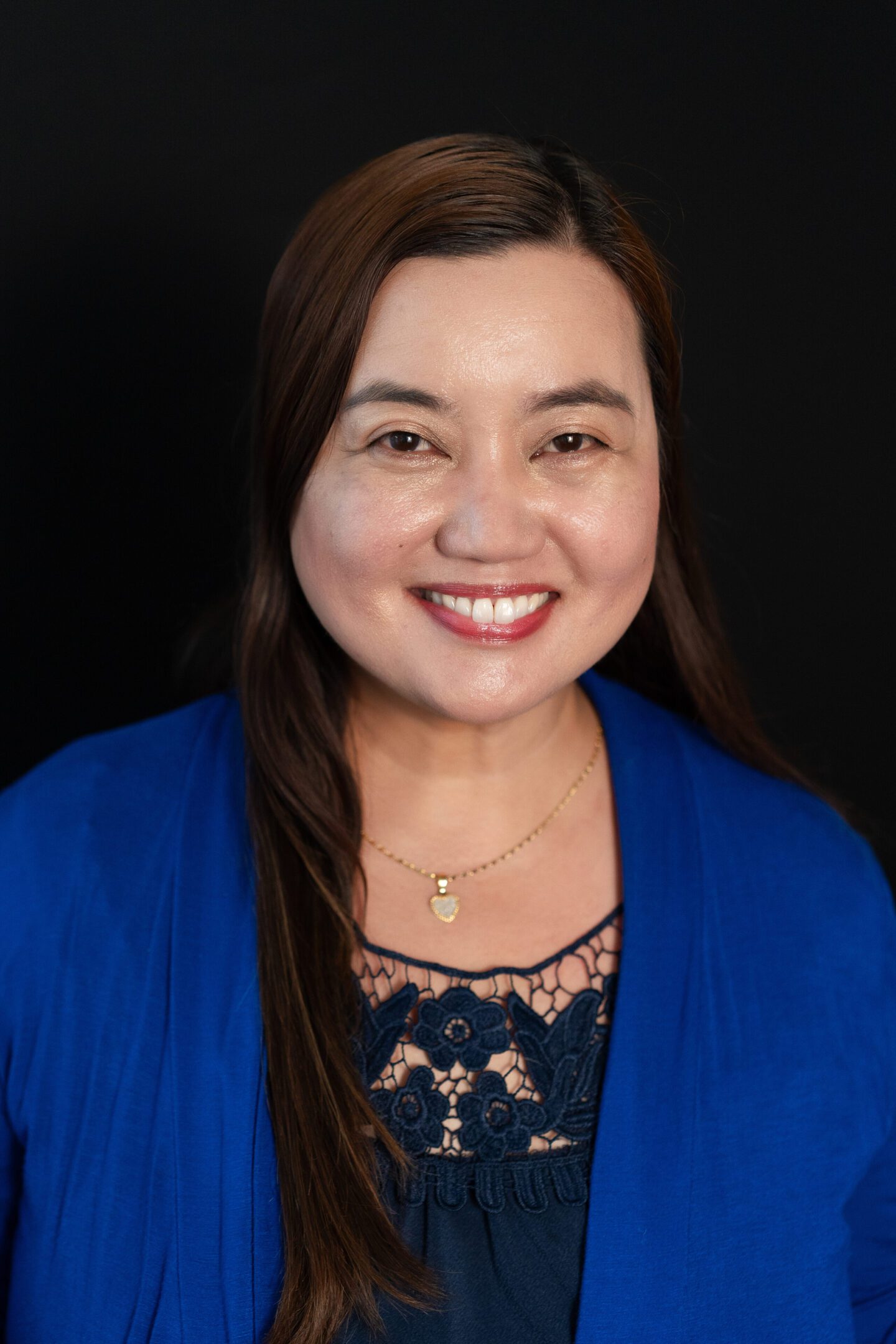 Smiling woman with long dark hair wearing a blue cardigan.